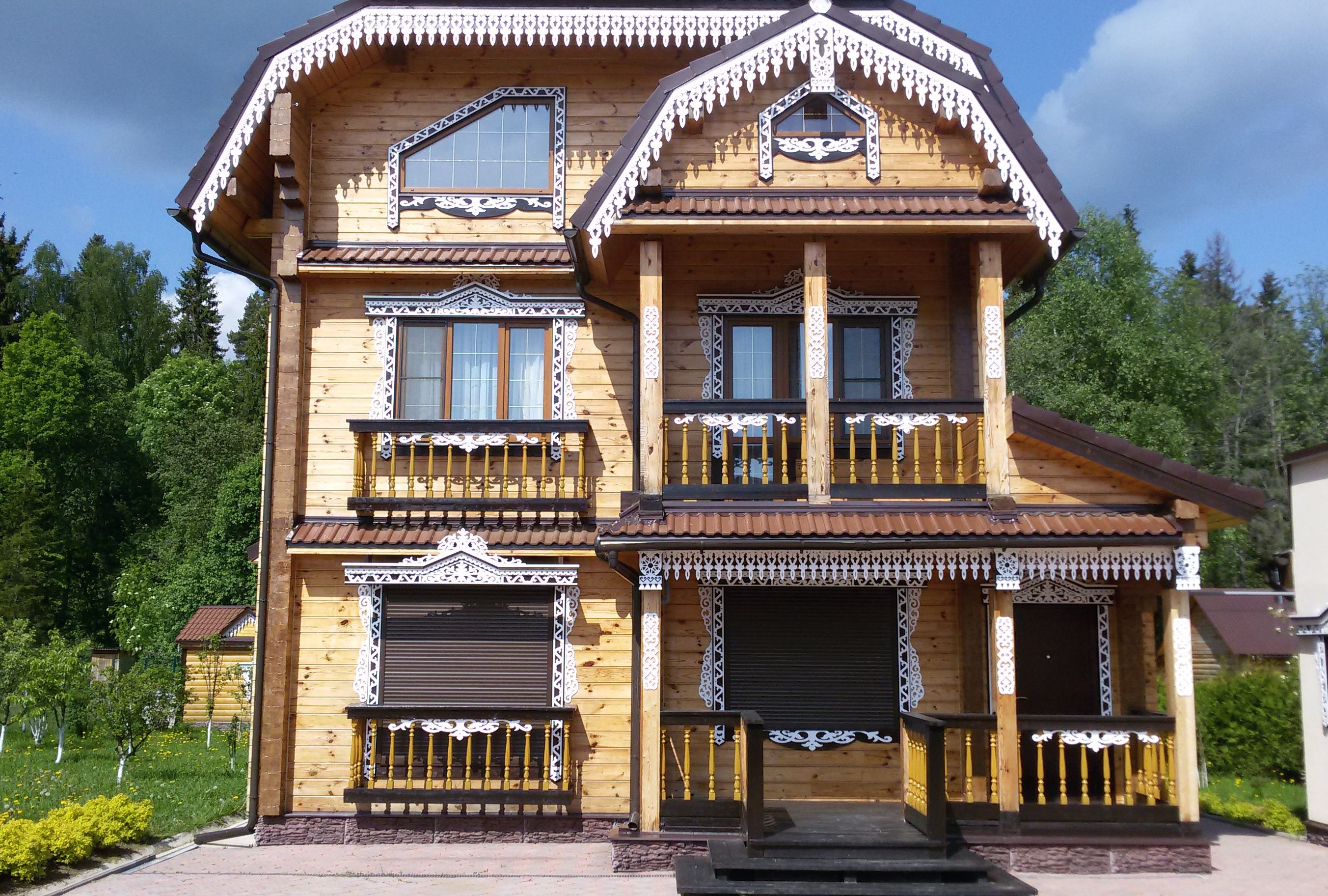 Белые резные наличники и карнизы на фасаде деревянного дома