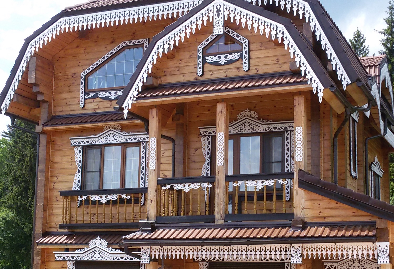 Белые ажурные резные наличники и карнизы на фасаде деревянного дома